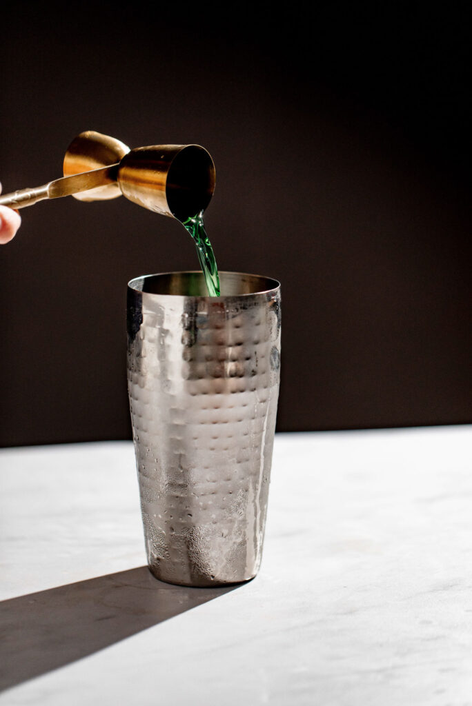Green Chartreuse being added to a cocktail shaker.